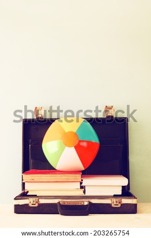 open briefcase with books and beach ball. sea in the background, filtered image.