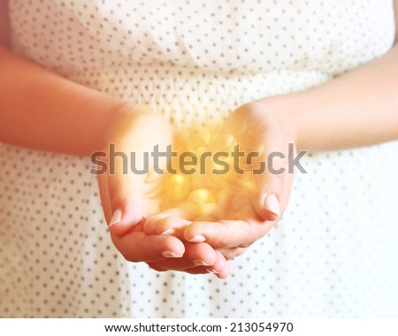 closeup of young woman hands. hands outstretched in cupped shape carring bright light. selective focus. retro toned image.