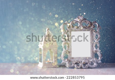 low key image of vintage antique classical frame and Burning candle on wooden table and glitter lights background . filtered image