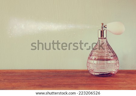 vintage antique perfume bottle with effect of perfume spray, on wooden table. retro filtered image