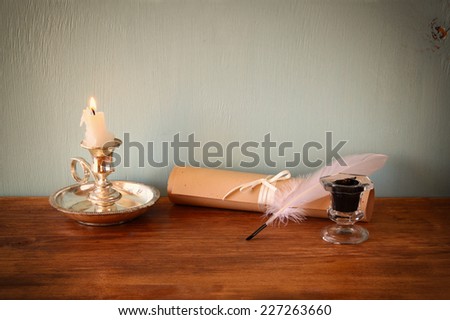 low key image of white Feather, inkwell and scroll on old wooden table