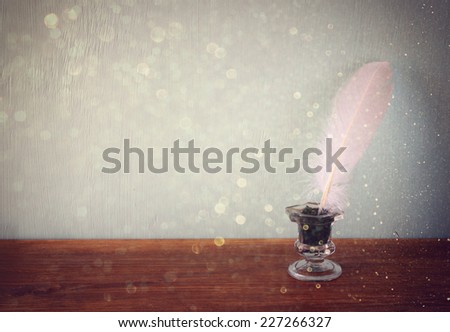low key image of white Feather, inkwell,  and glitter lights background on old wooden table