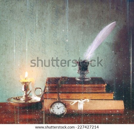 low key image of white Feather, inkwell, old books and candle with glitter lights background on old wooden table
