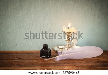 low key image of white Feather, inkwell, and candle on old wooden table. filtered image