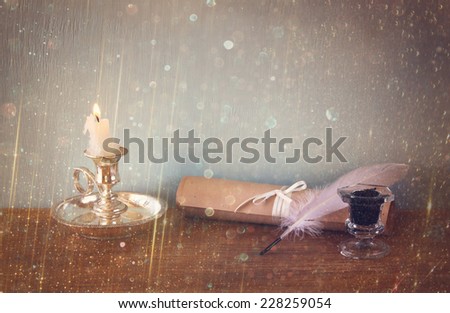 low key image of white Feather, inkwell, scroll and glitter lights background on old wooden table