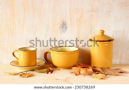 set of coffee mugs and old jar over wooden rustic table and autumn leaves