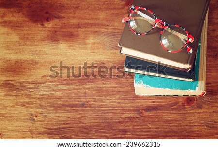 top view of old book stack and old glasses over wooden table. filtered image