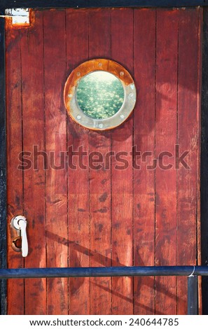 picture of old ship door with a round window and the sea reflected through it