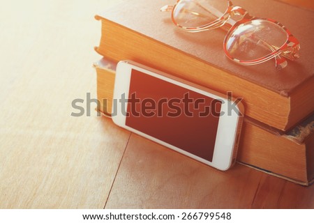 reading glasses, stack of  old books and smart phone over wooden table, retro filtered image