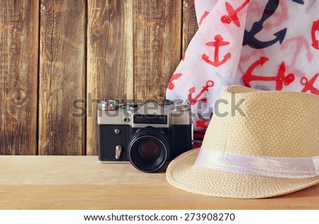 fedora hat, scarf and old vintage camera over wooden table. relaxation or vacation concept
