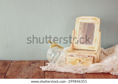 vintage pearls , antique wooden jewelry box with mirror and perfume bottle on wooden table. filtered image