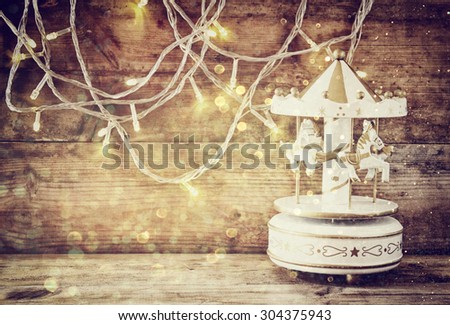 abstract image of old vintage white carousel horses with garland gold lights on wooden table. retro filtered image with glitter overlay