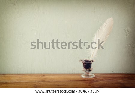 photo of white Feather and inkwell on old wooden table. retro filtered image