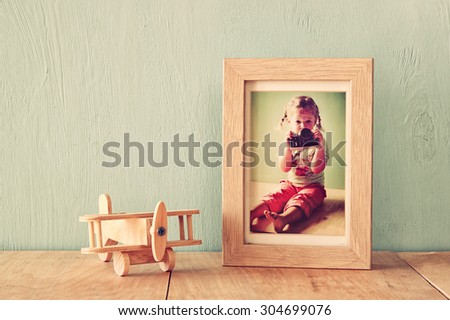 wooden airplane toy over wood table next to photo frame with kid\'s old photography. retro filtered image