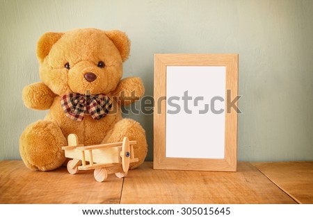 wooden airplane toy and teddy bear over wood table next to blank photo frame. retro filtered image. ready to place photography