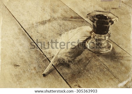 photo of white Feather and inkwell on old wooden table. retro filtered image, black and white style photo