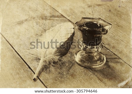 photo of white Feather and inkwell on old wooden table. retro filtered image, black and white style photo