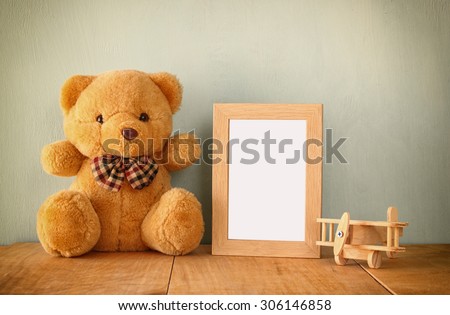 wooden airplane toy and teddy bear over wood table next to blank photo frame. retro filtered image. ready to place photography