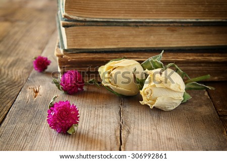 selective focus image of dry rose, and old vintage books on wooden table. retro filtered image