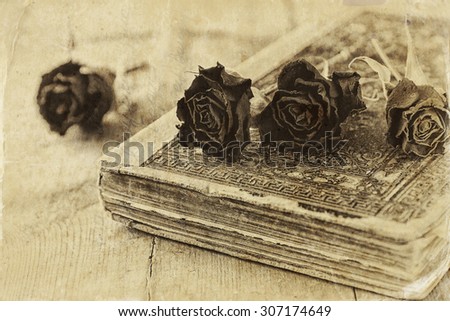 selective focus image of dry red roses and old vintage books on wooden table. black and white old style photo