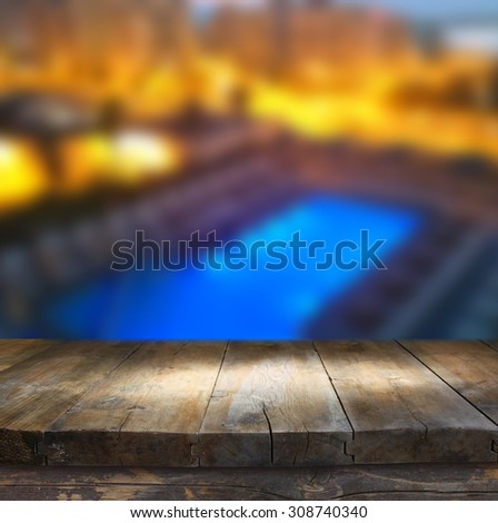 wood board table in front of rich hotel pool at night. Ready for product display montages