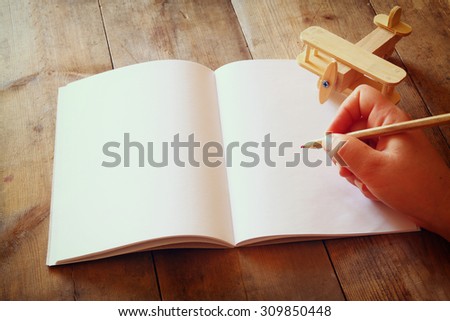 open blank notebook and woman hands next to toy aeroplane on wooden table. retro style filtered image