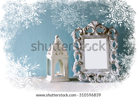 abstract image of vintage antique classical frame and old lantern on wooden table with snowflakes overlay