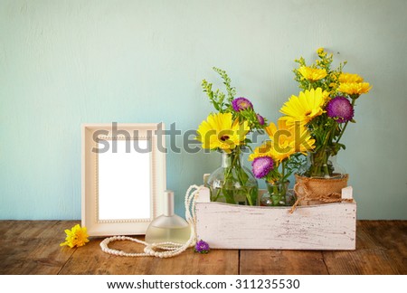 summer bouquet of flowers next to blank vintage photography frame on the wooden table with mint background. vintage filtered image