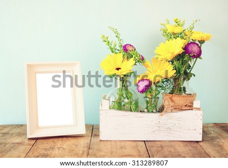 summer bouquet of flowers next to blank vintage photography frame on the wooden table with mint background. vintage filtered image