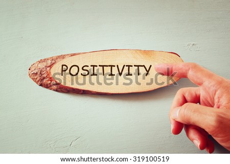 image of male hand pointing at wooden sign with the word positivity