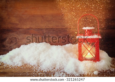 christmas background with red lantern ans snow over wooden background with glitter overlay