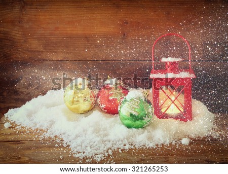 christmas background with red lantern, bauble and snow over wooden background. glitter overlay