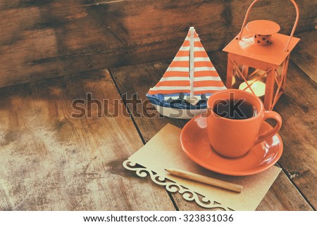 red cup of tea and letter paper next to vintage decorative boat and lantern on wooden old table. retro filtered image