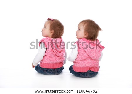 Adorable baby twin girl sisters wearing blue jeans and pink tops with pretty bows in their hair isolated on a white seamless background
