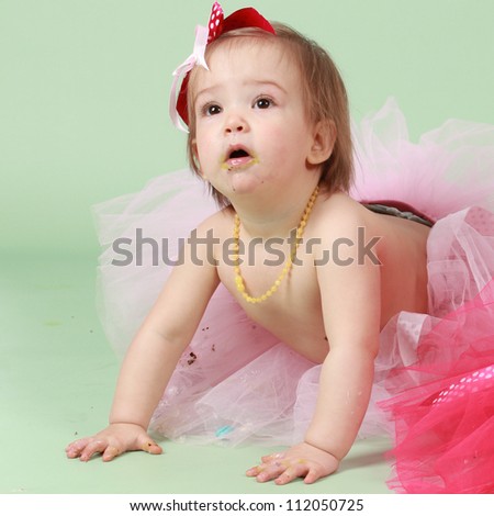 Baby girl on green seamless background wearing tutu and bows in the hair enjoying herself celebrating her birthday party