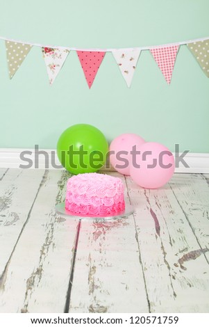 Beautifully designed pink ombre butter icing birthday party cake on distressed wooden white washed floor and green background with green and pick flag bunting and balloons