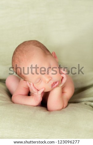 Sleepy newborn baby girl or boy sleeping with chin on hands lying on green soft blanket