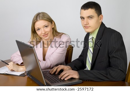 Man and woman at the office desk. There\'s laptop and notepad on it. Man\'s hands on the keyboard.
