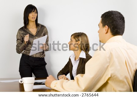 Two women and a man are at the table. One of the women's standing and talking to the rest of people.