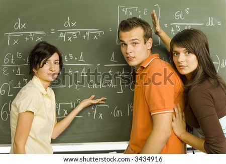 Small group of teenagers standing in front of blackboard. Trying to understand exercise on blackboard. Looking at camera, side view