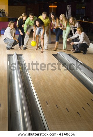 Large group of teenagers standing and crouching in bowling alley. One person is holding ball, others are waiting for strike