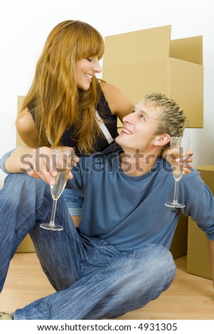 Young couple sitting on the floor in flat. They\'re looking happy. Celebrating removal with champagne. Looking at each other