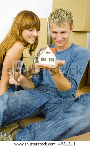 Young couple sitting on the floor in flat. They\'re looking happy. Man is holding house miniature and they\'re looking at it