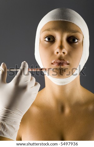 Young, beautiful woman with bandage on head. Somebody is injecting something in her\'s lips. Front view, gray background