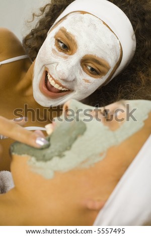 Happy young women lying on towel putting puryfing mask.