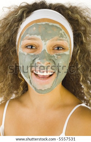 Young happy woman with green purifying mask. She's looking at camera.