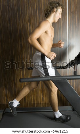 Young man with naked chest running on track in gym. Whole body, side view