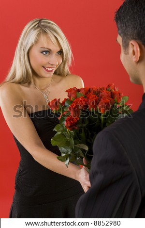 Young man in suit is giving flowers to beautiful, smiling woman. The man is standing back