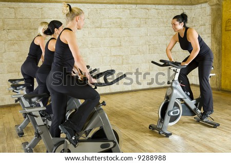 The group of women in dark sportswear training on exercise bike at the gym. Side view.