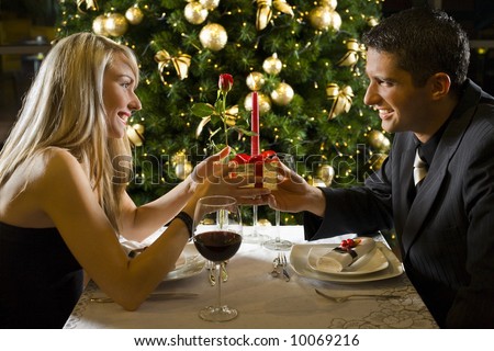 Couple at restaurant on dinner party. They giving each other a present.